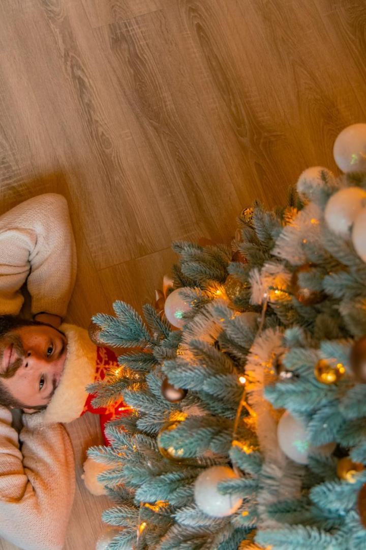 Mann liegt mit Weihnachtshaube und beigen Pullover unter einem Weihnachtsbaum