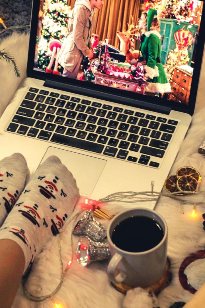 Frau schaut Weihnachtsfilme auf Laptop umgeben von Geschenken