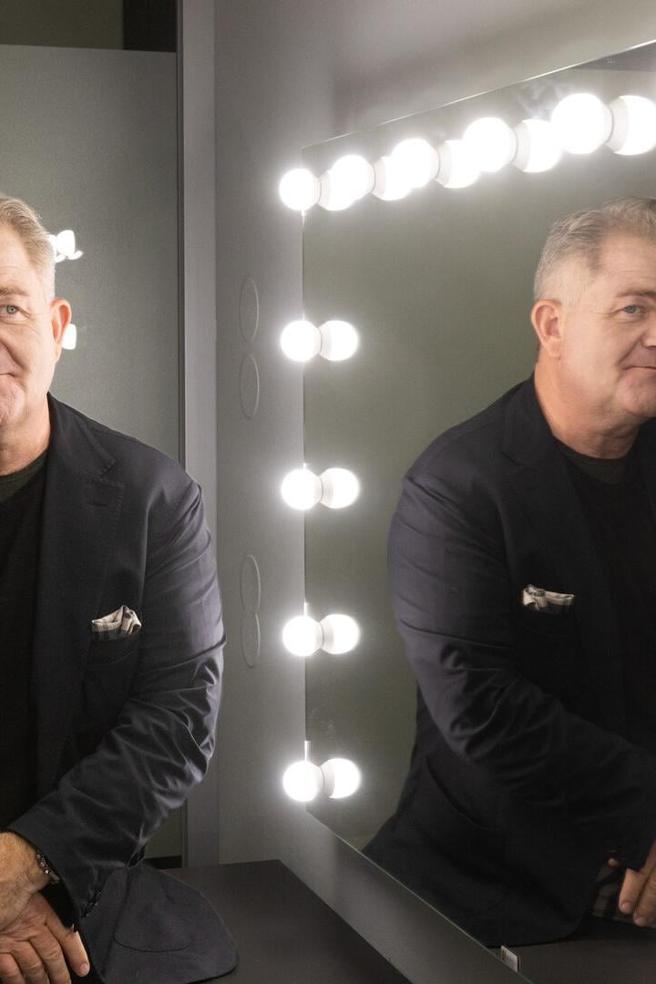 Ein Mann sitzt vor einem beleuchteten Spiegel und schaut nachdenklich, sein Spiegelbild ist deutlich zu sehen.