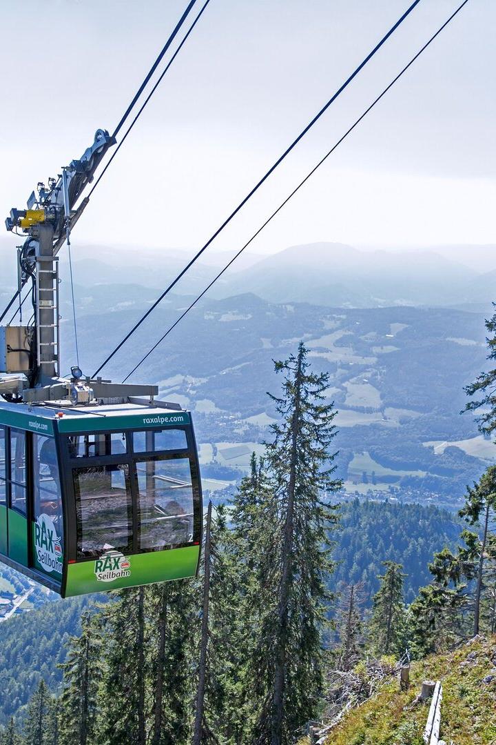 Eine grüne Rax-Seilbahn schwebt vor einer Berglandschaft.