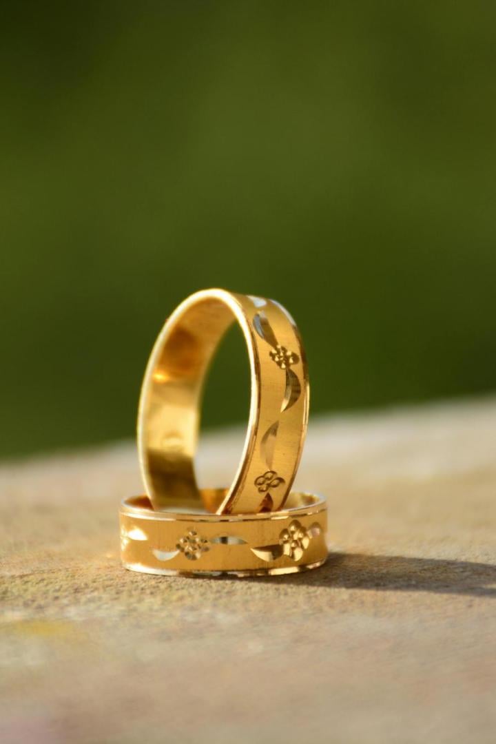 Zwei goldene Ringe mit eingravierten Blumenmustern stehen auf einer Oberfläche vor unscharfem grünem Hintergrund.
