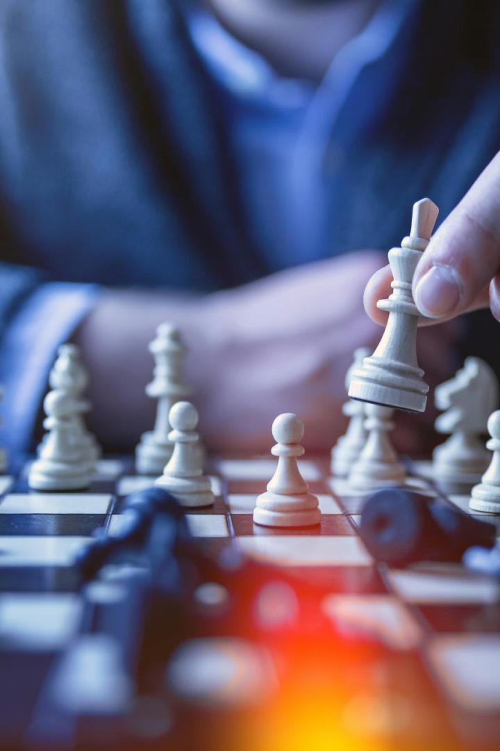 Mann hält weiße Schachfigur in der Hand über einem Schachbrett