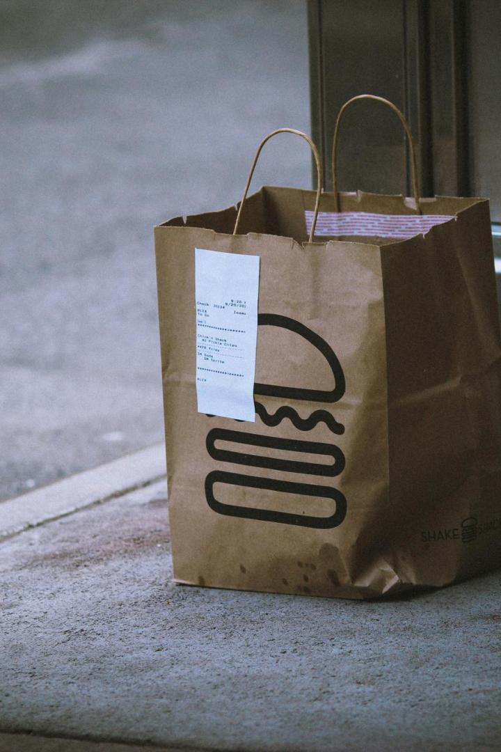 braune Papiertüte mit Burger-Symbol steht auf grauem Betonboden