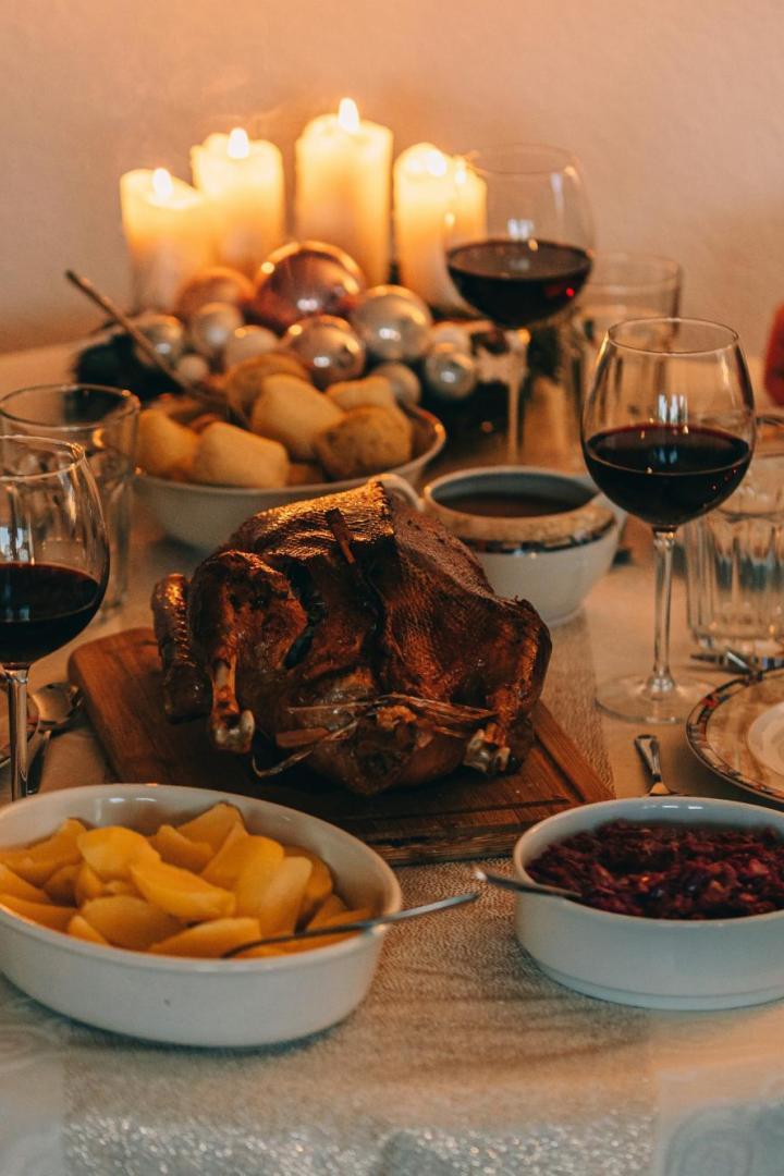 Festlich gedeckter Tisch mit Gänsebraten, Rotwein, Kartoffeln, Rotkohl, Kerzen und zwei Personen beim Abendessen.