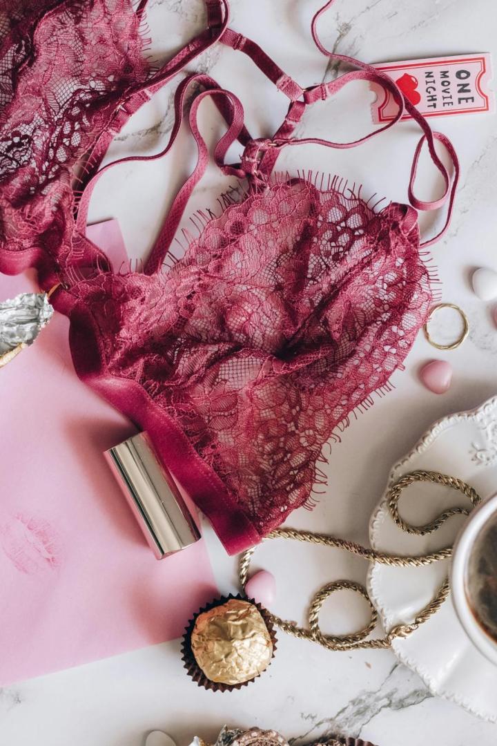 Spitzen-BH in Rot liegt neben Pralinen, Lippenstift, Schmuck und einer Tasse Kaffee auf einem Marmortisch, passend zum Silvesterbrauch für Glück im neuen Jahr.