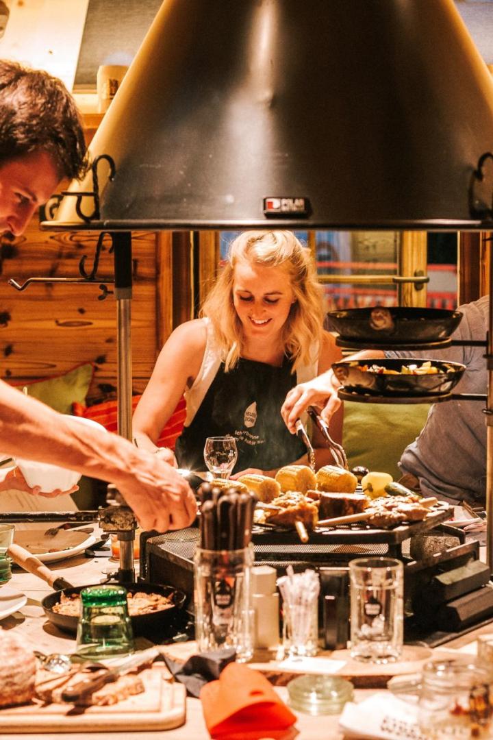 Menschen grillen gemeinsam an einem Tisch in eine Holzhütte.