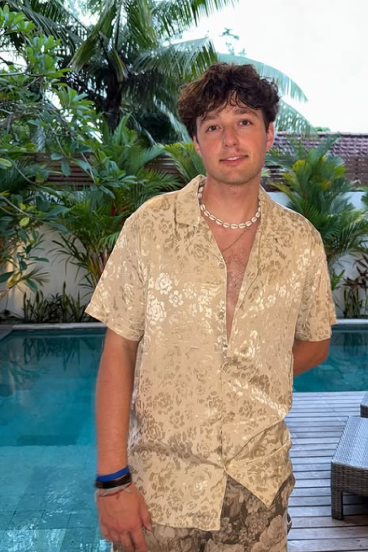 Tucke Genal steht in einem gold schimmernden Hemd vor einem Pool.