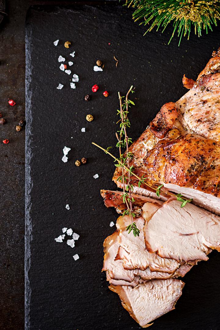 Roasted sliced Christmas ham of turkey on dark rustic background. Top view. Festival food.