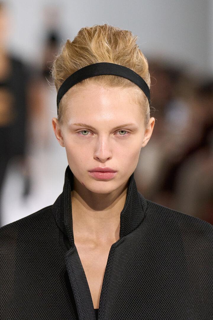 Eine sehr dezent geschminkte Frau im schwarzen Blazer mit schwarzem Haarband