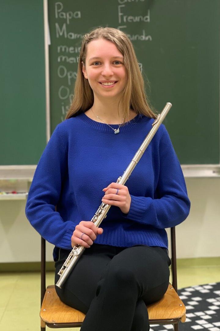 Kathrin Holzer sitzt vor einer Schultafel mit einer Querflöte in der Hand.