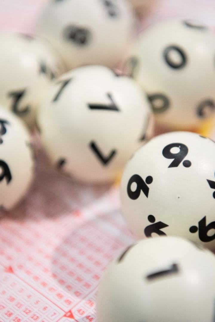 Mehrere weiße nummerierte Lotto-Kugeln liegen auf einem Lottoschein.