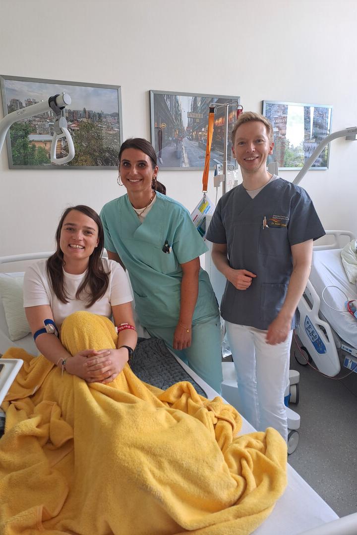 Katrin Teufel mit Besuchern in einem Bett im Krankenhaus.