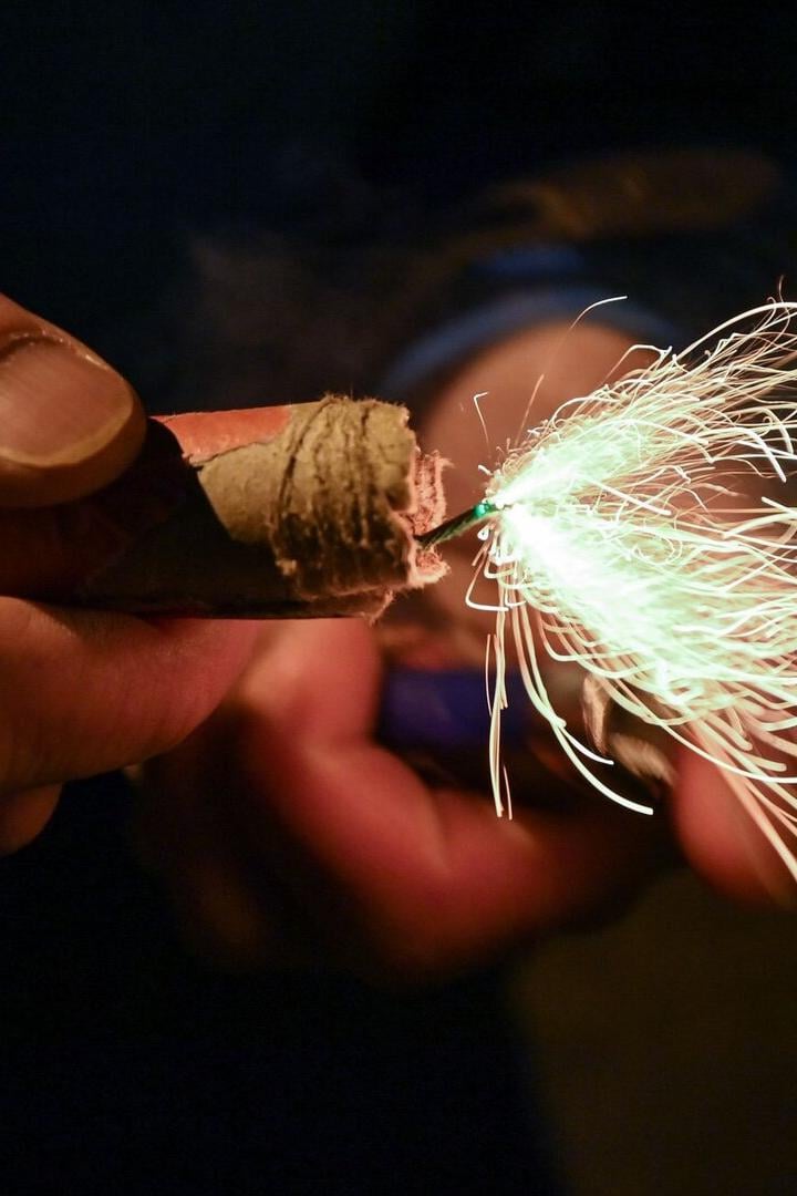 Eine Hand hält einen brennenden Böller, von dem Funken sprühen.