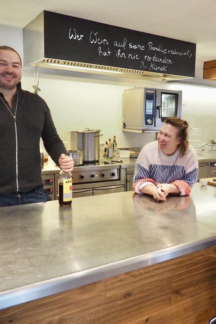 Drei Personen stehen und sitzen lächelnd an einer Küchentheke mit Getränken.