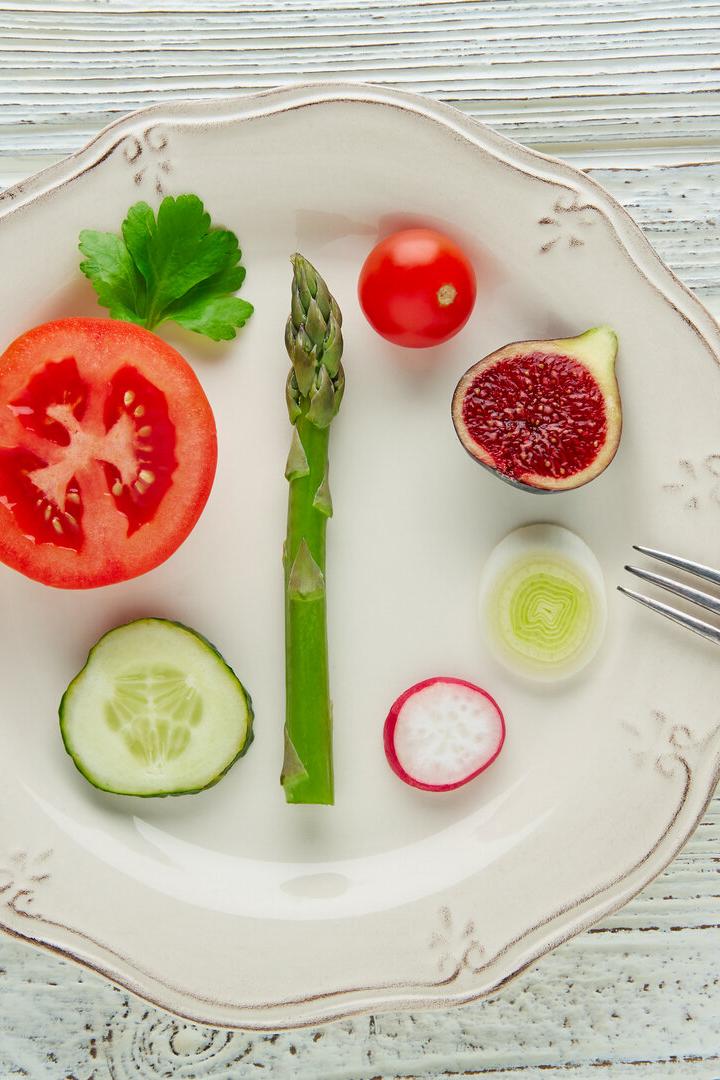 Verschiedene Gemüsescheiben, eine Feige und ein Spargel liegen dekorativ auf einem weißen Teller mit einer kleinen Gabel.