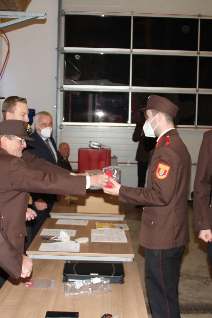 Feuerwehrmänner in Uniform übergeben sich gegenseitig ein verpacktes Geschenk.