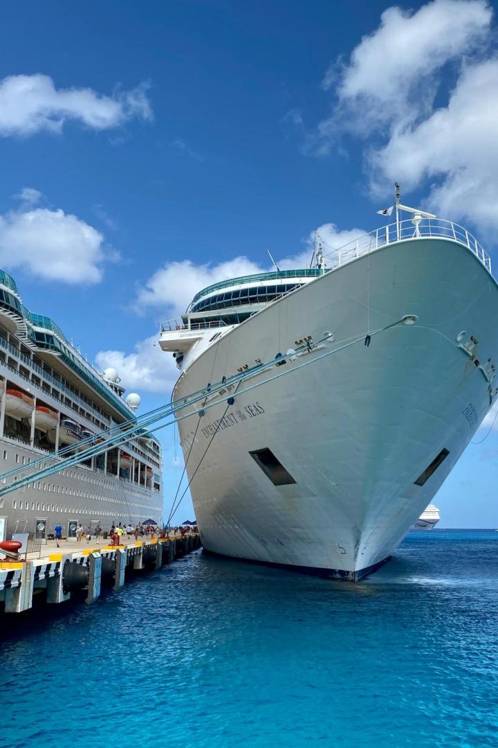 Zwei große Kreuzfahrtschiffe liegen bei sonnigem Wetter an einem Pier im türkisblauen Wasser.