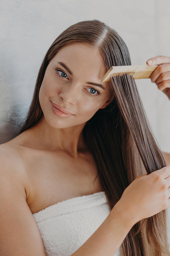 Eine junge Frau mit einem Handtuch um den Körper kämmt ihr langes, braunes Haar.