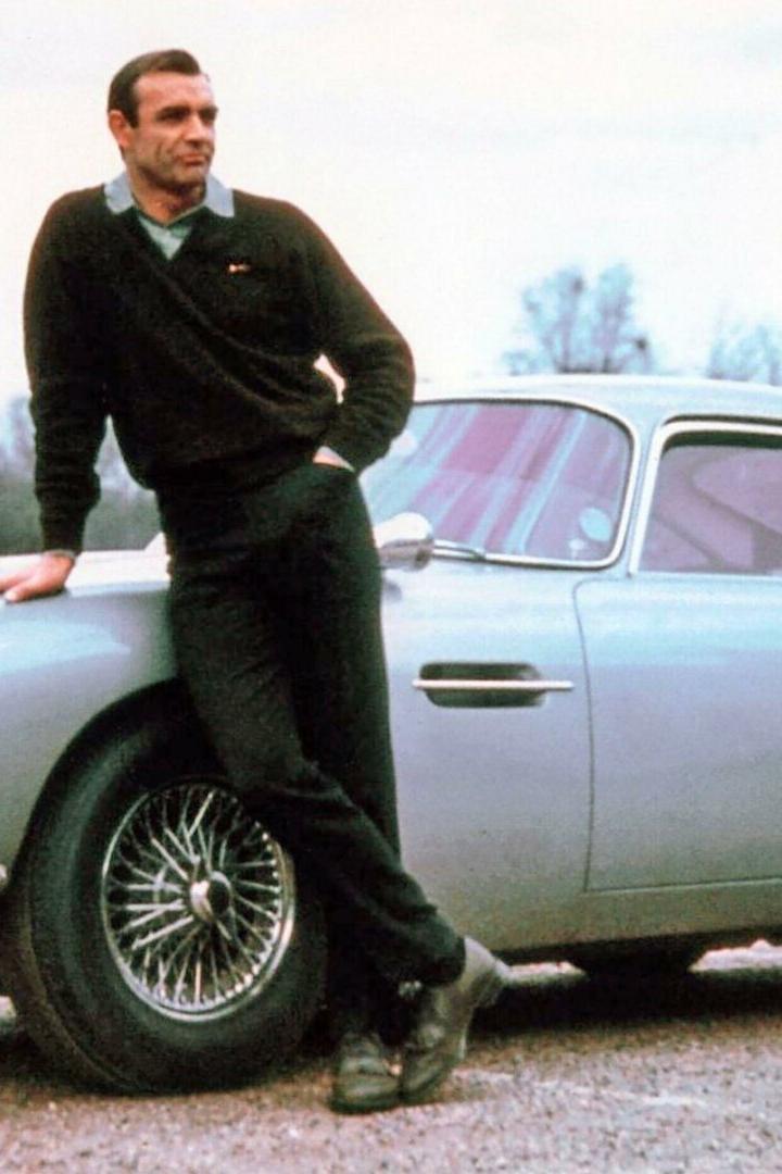 Sean Connery lehnt lässig an einem silbernen Aston Martin DB5 mit dem Kennzeichen BMT 216A.