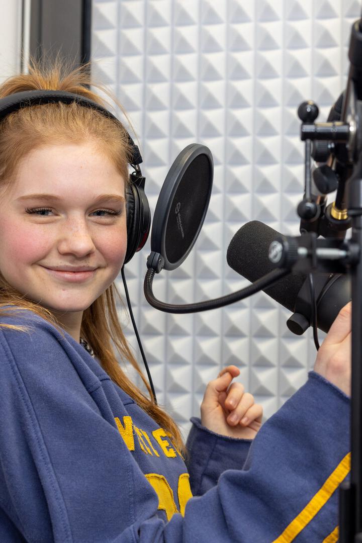 Eine junge Frau mit Kopfhörern lächelt in einem Tonstudio vor einem Mikrofon.