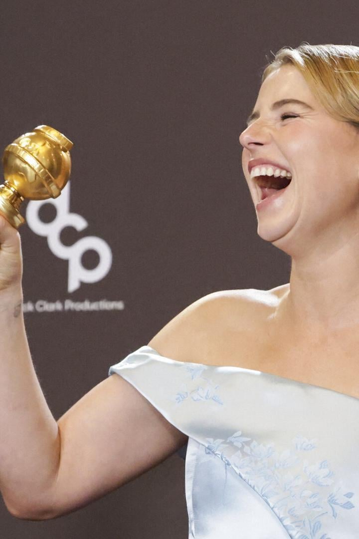 Eine Frau im eleganten Kleid hält lachend eine goldene Trophäe in der Hand.
