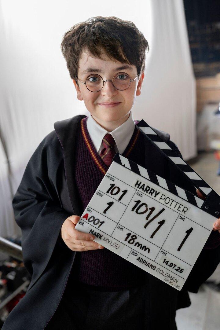 Ein junger Schauspieler im Harry-Potter-Kostüm hält eine Filmklappe mit der Aufschrift "Harry Potter, Episode 101".