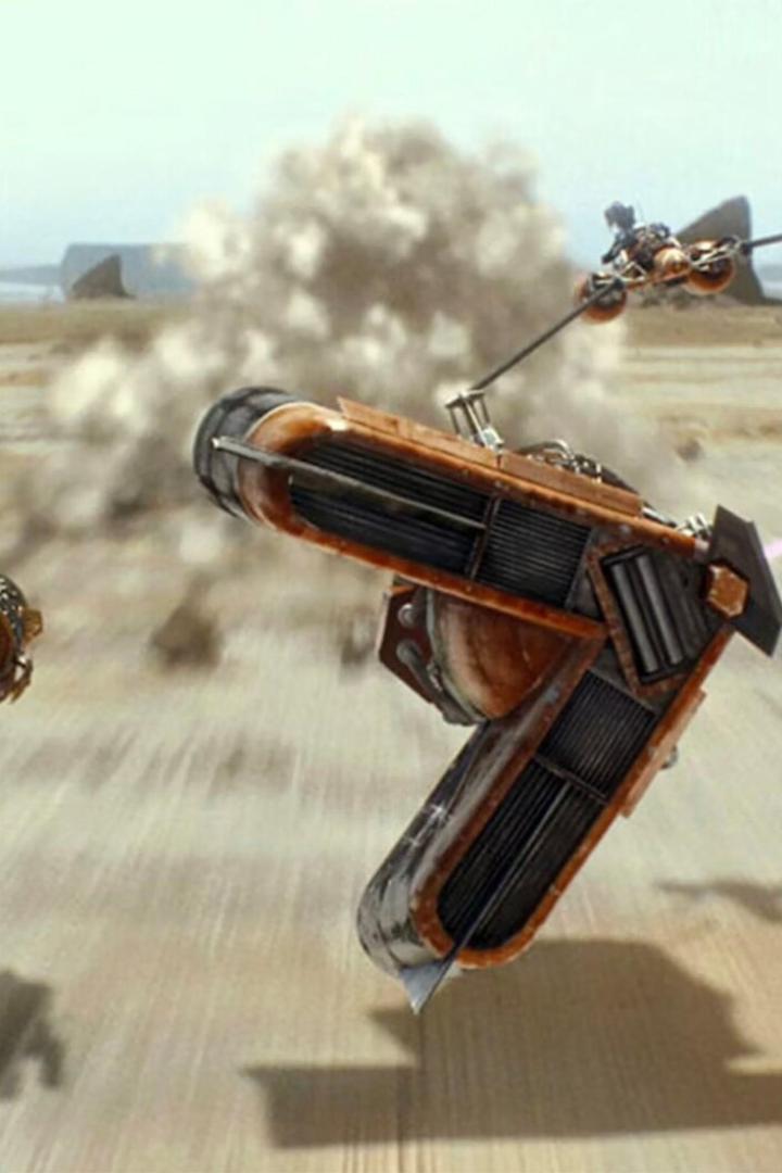 Zwei futuristische Rennfahrzeuge rasen mit hoher Geschwindigkeit über eine sandige Wüstenlandschaft.