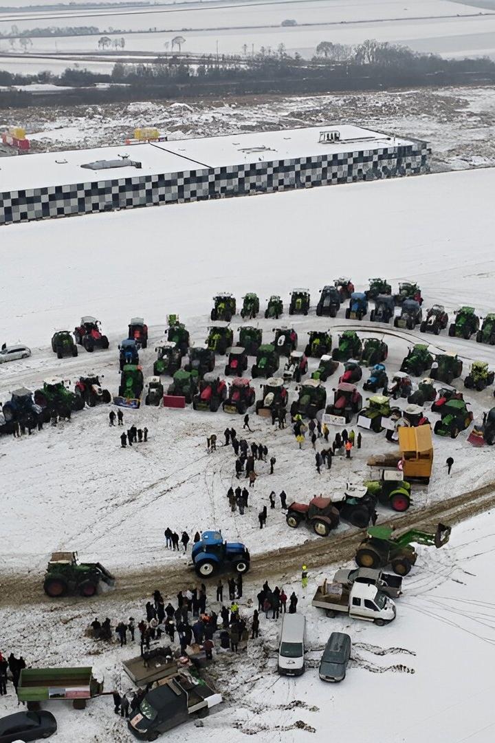 Viele Traktoren und Menschen versammeln sich auf einem verschneiten Feld in einer großen Kreisformation.