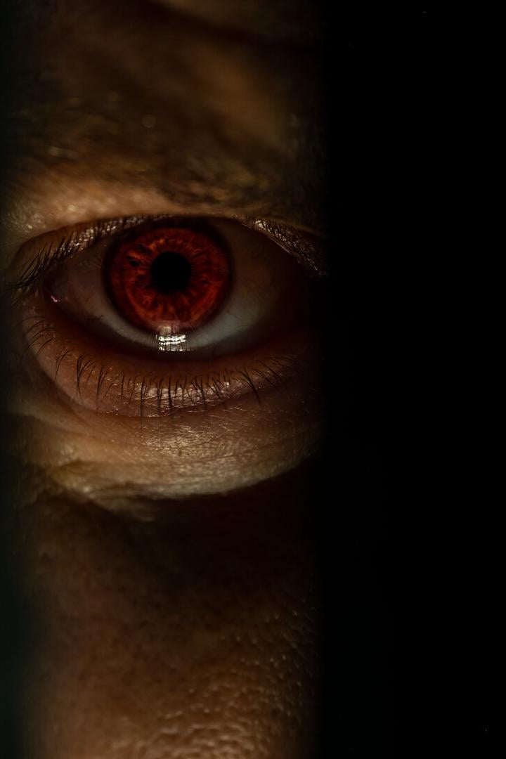 Ein rotes menschliches Auge blickt durch einen schmalen dunklen Spalt.