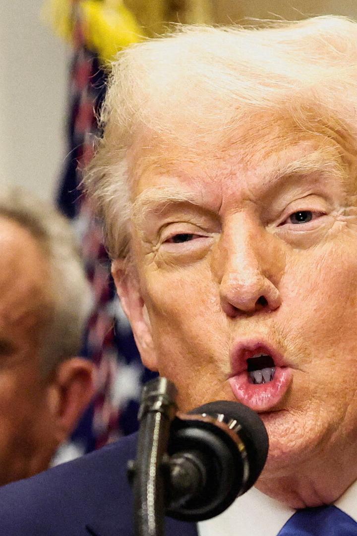 Donald Trump spricht am Mikrofon, eine weitere Person ist im Hintergrund zu sehen.