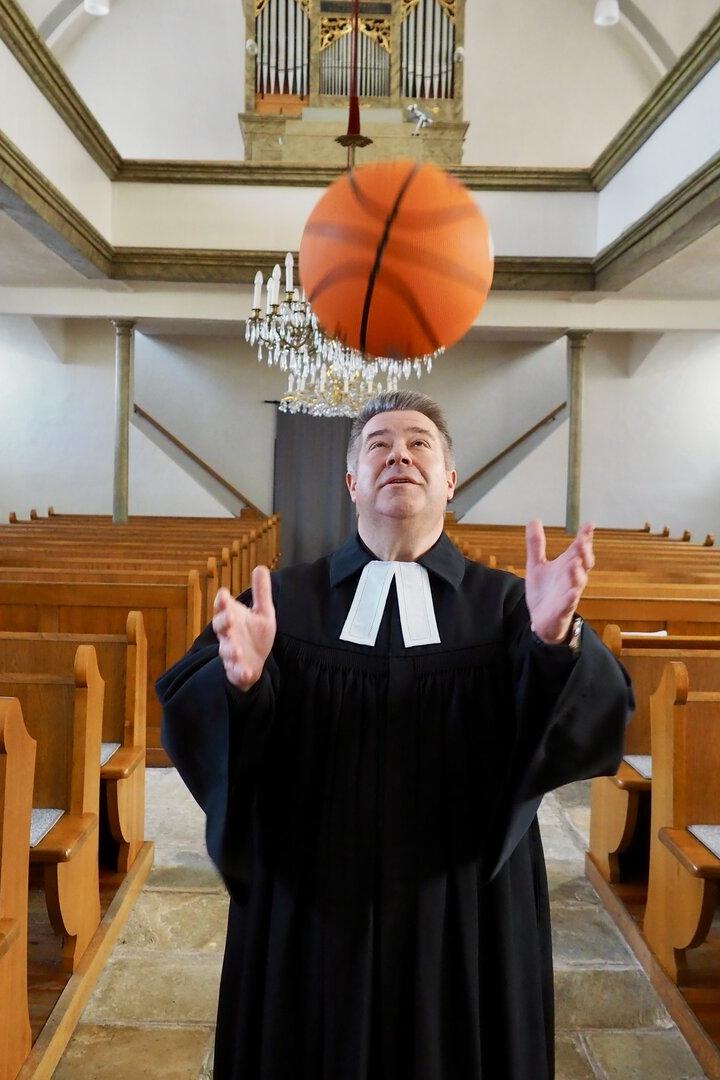 Ein Pfarrer jongliert in einer Kirche mit einem Basketball.
