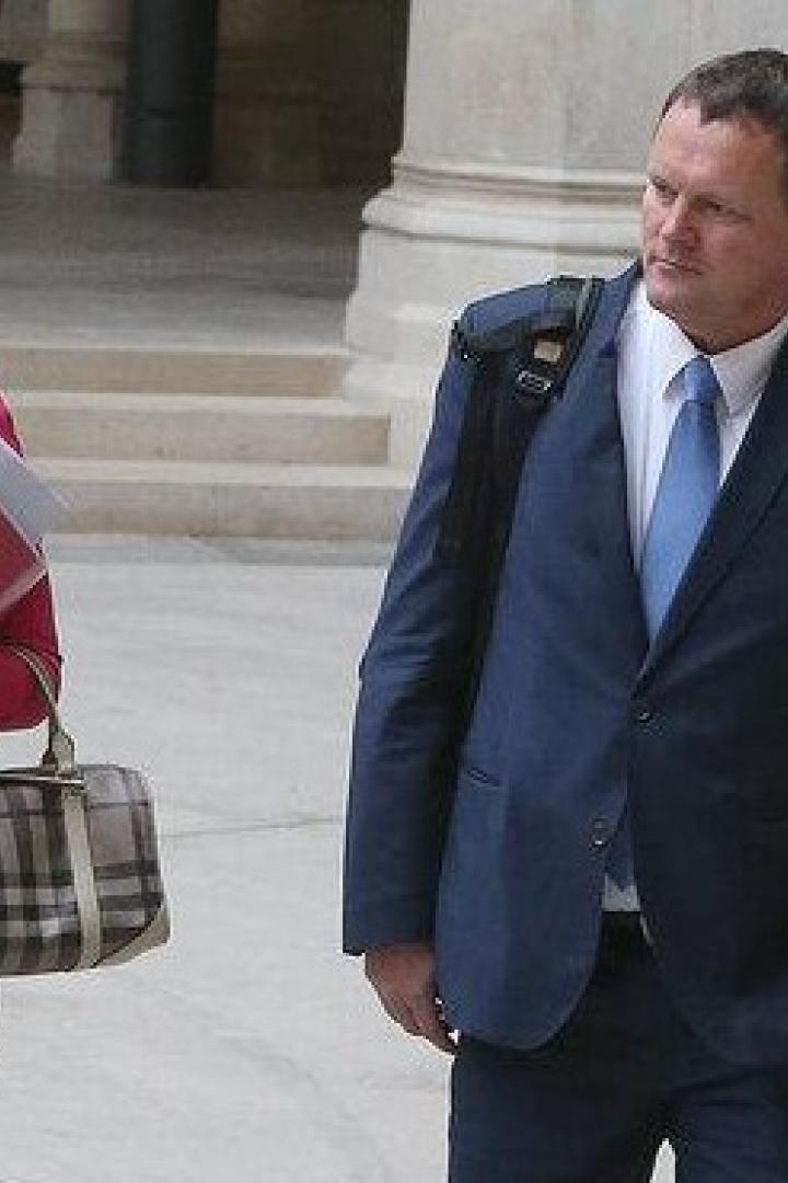 Fünf Personen, darunter Taborsky und Hungerländer,  in Businesskleidung gehen mit Aktenmappen durch einen historischen Arkadengang.