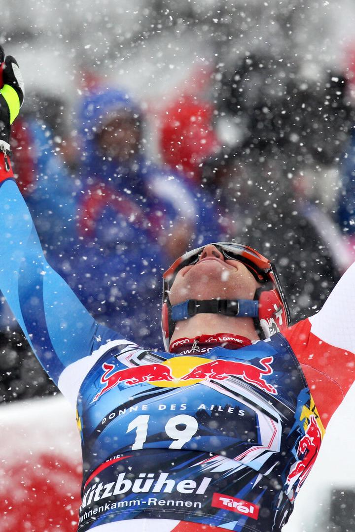 Ein Skirennläufer mit Startnummer 19 jubelt mit erhobenen Armen im Schneefall, im Hintergrund Zuschauer.