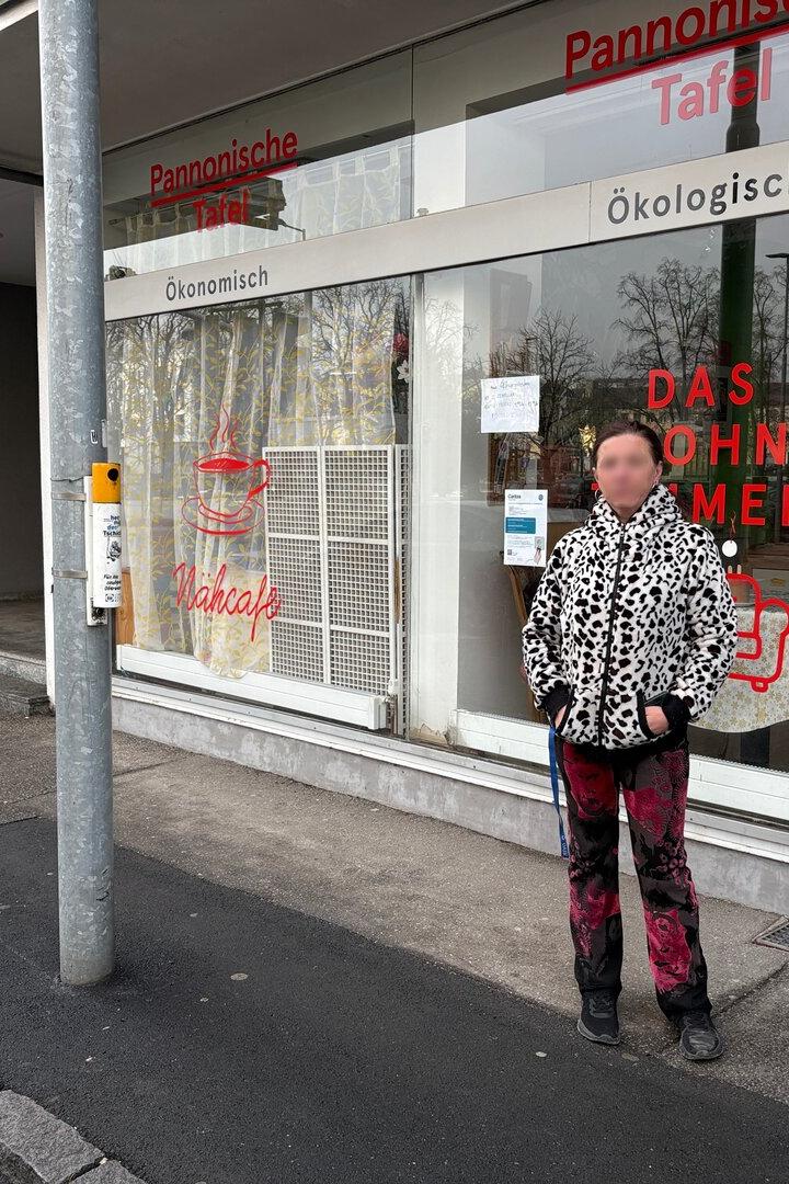 Eine Person steht vor einem Schaufenster mit der Aufschrift „Pannonische Tafel“ und bunten Bildern an der Scheibe.