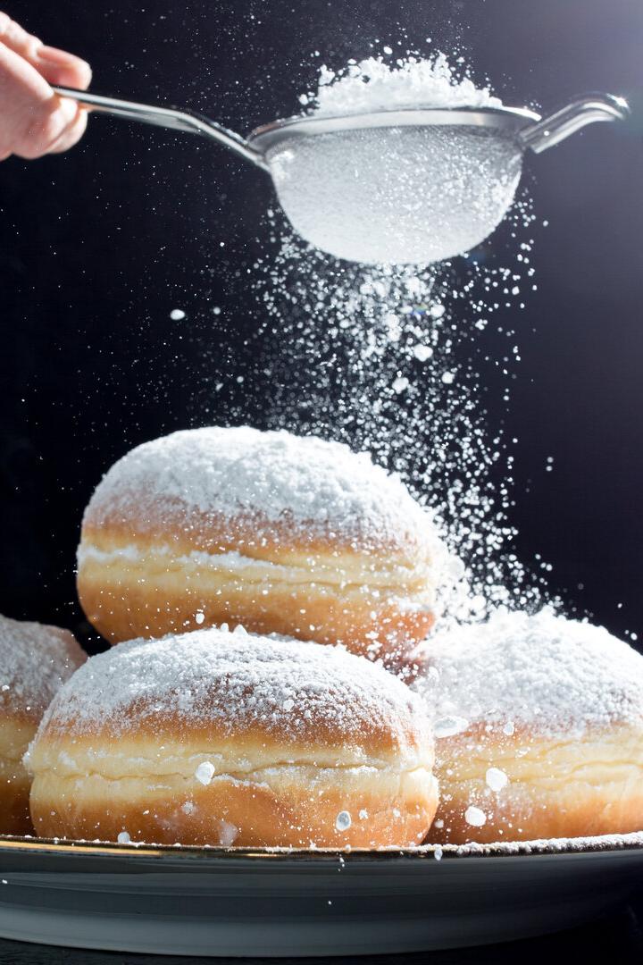 Ein Teller Krapfen wird mit Puderzucker bestreut.