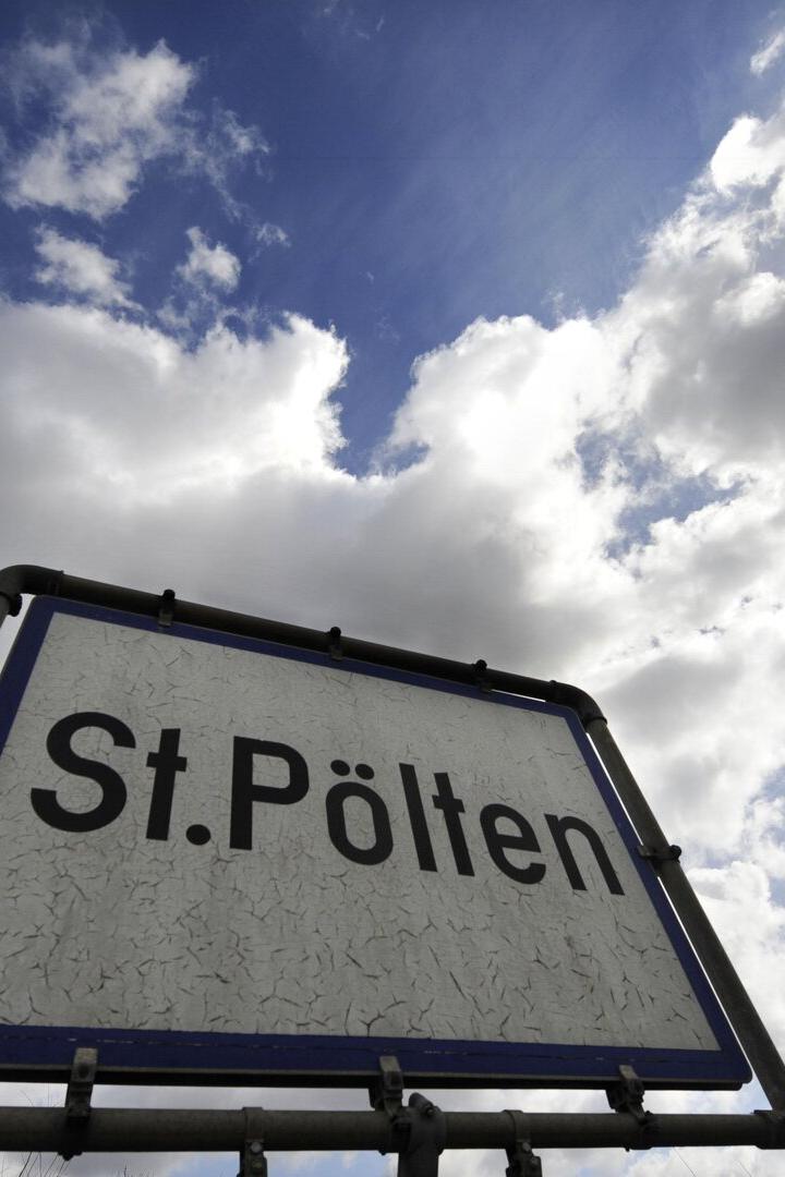 Ein Ortsschild mit der Aufschrift „St. Pölten“ vor einem Himmel mit vielen Wolken.