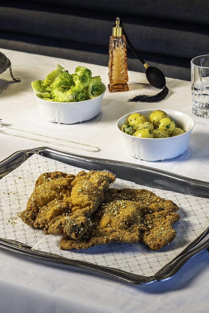 Auf einem gedeckten Tisch stehen Schnitzel auf einem Serviertablett, dazu Salat, Kartoffeln, Kaviar und Getränke.