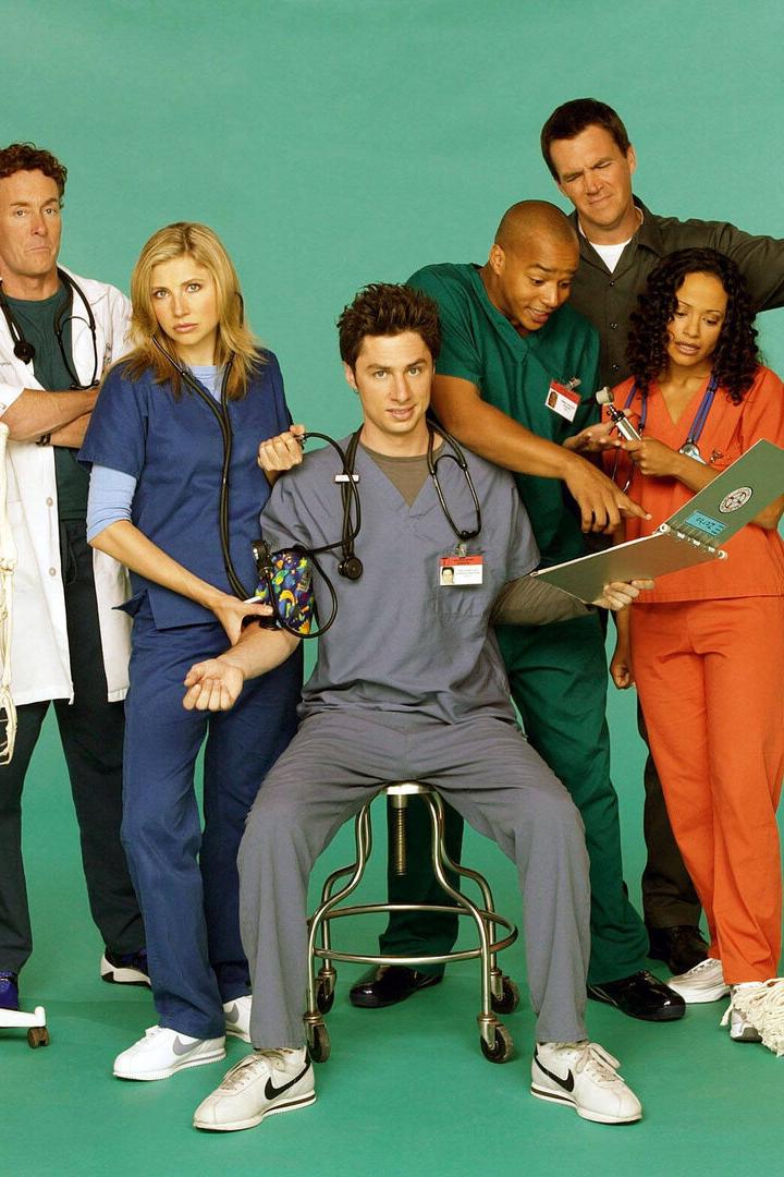 Sieben Personen in Krankenhauskleidung stehen zusammen, eine Person sitzt, ein Skelett und ein Wischmopp sind zu sehen.