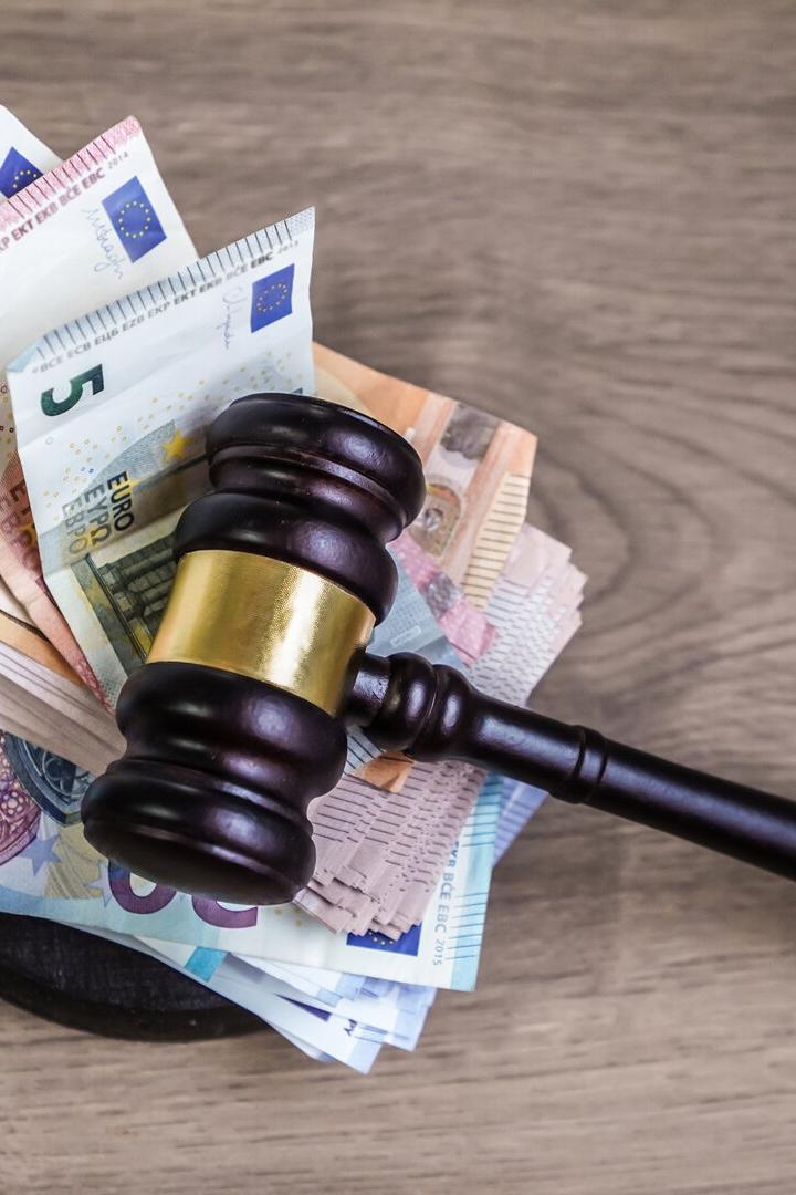 Ein Richterhammer liegt auf einem Stapel verschiedener Euro-Geldscheine auf einer Holzoberfläche.