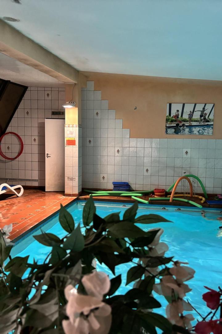 Ein Mann schwimmt in einem hell erleuchteten Innenpool mit Schwimmhilfen am Beckenrand.
