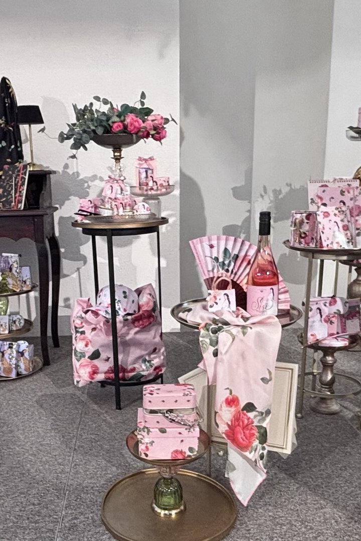 Verschiedene rosa und floral verzierte Geschenkartikel, Taschen, Schachteln und eine Flasche Roséwein sind dekorativ arrangiert.