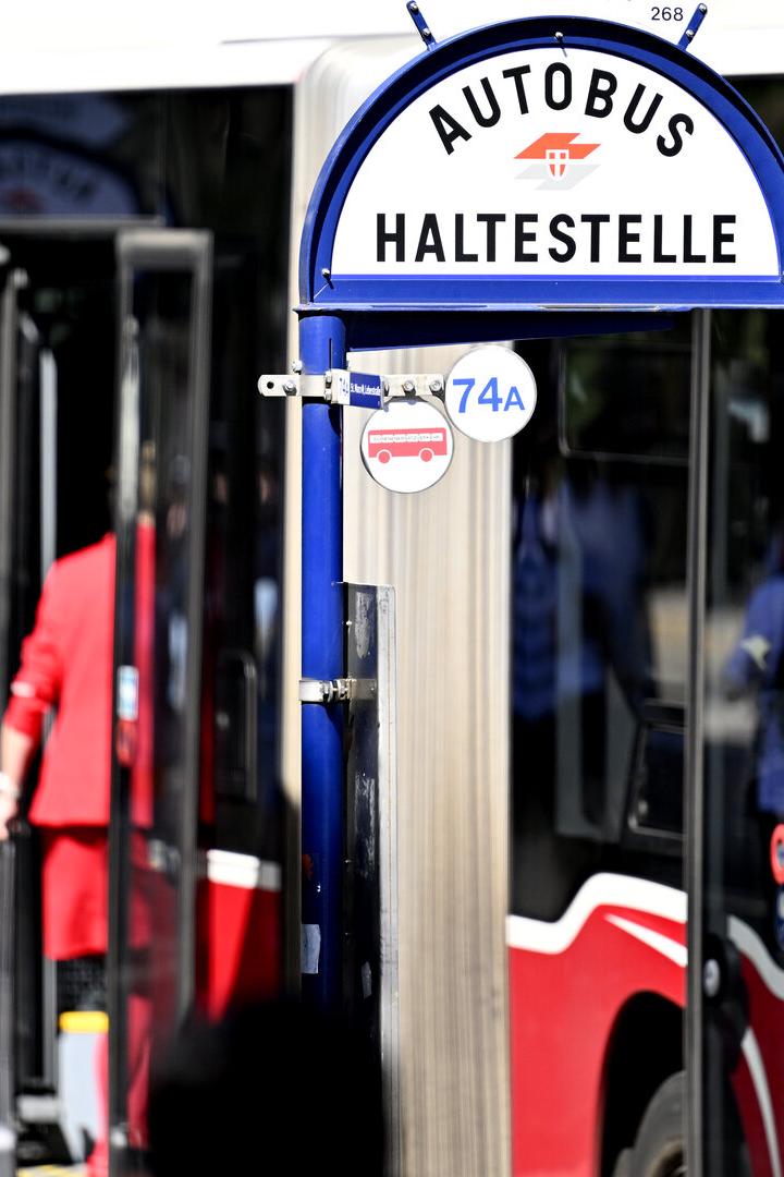 Ein blaues Haltestellenschild für den Autobus 74A steht vor einem roten Bus, eine Person steigt ein.