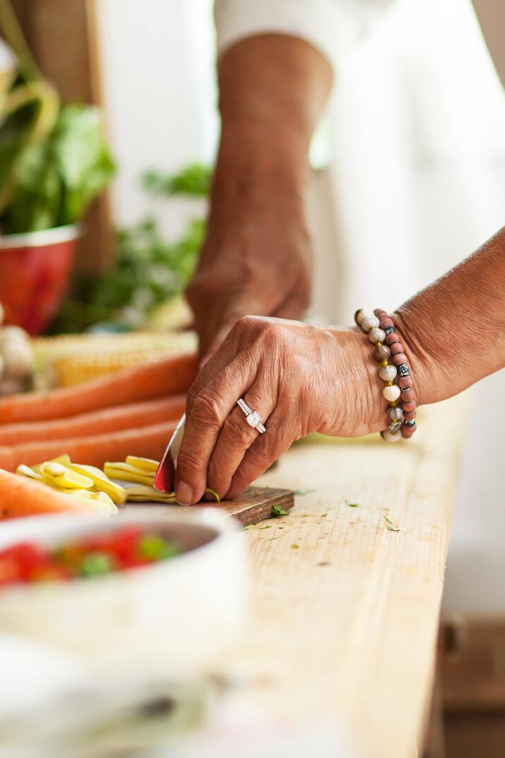 Eine Person schneidet frisches Gemüse auf einem Holztisch, umgeben von weiteren Gemüsesorten.