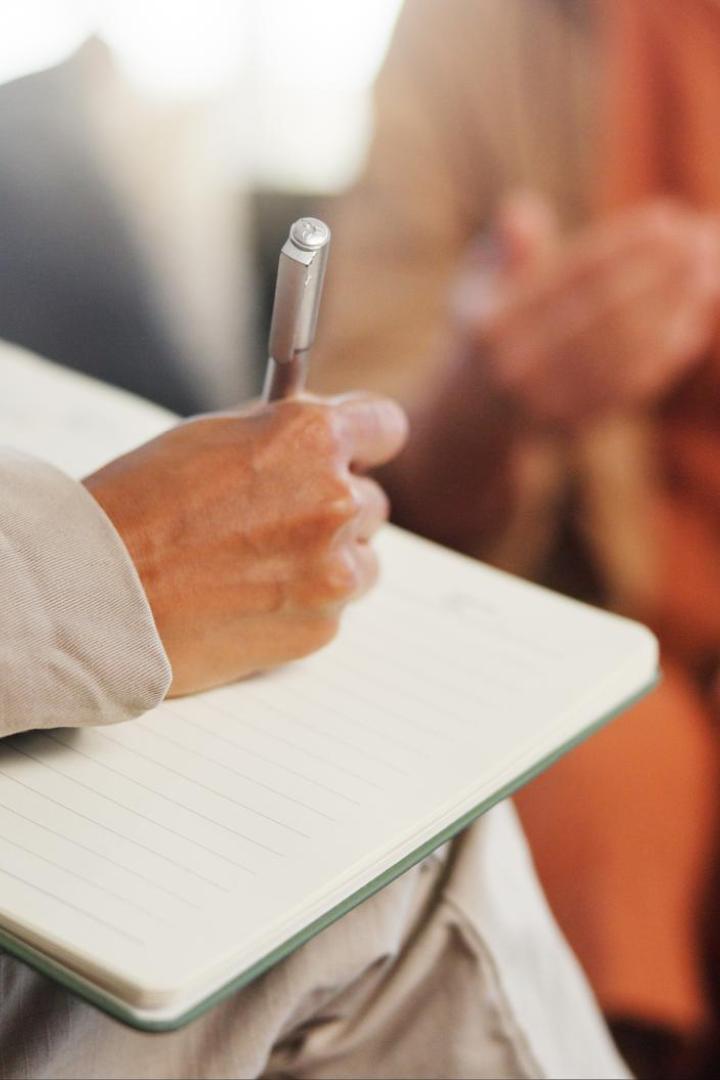 Ein Therapeut schreibt mit einem Stift in ein Notizbuch, die andere Person gestikuliert mit den Händen.