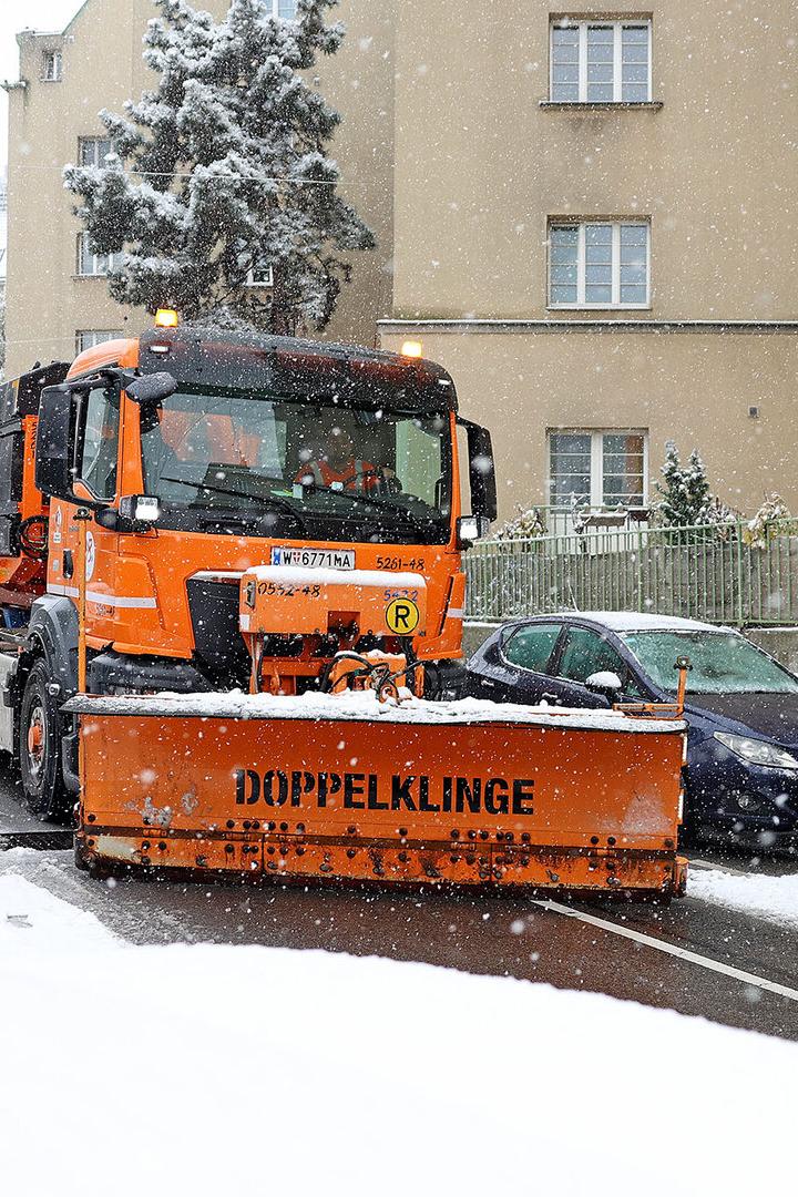 Ein orangenes Räumfahrzeug der MA 48 fährt durch eine schneebedeckte Gasse.