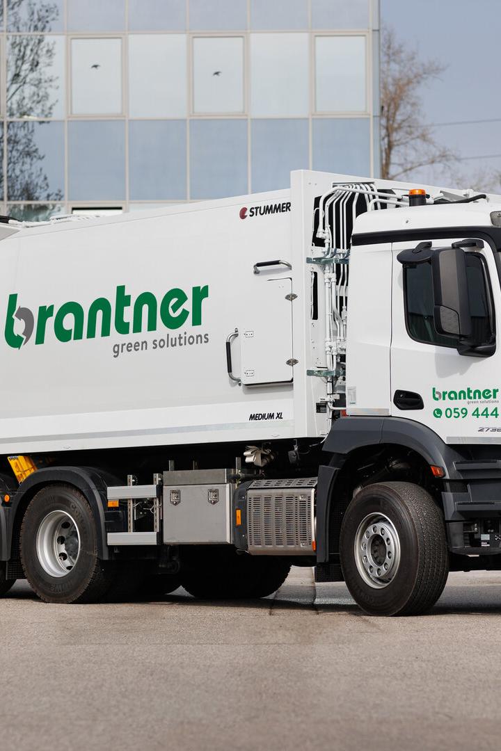 Weißer Müllwagen der Marke Brantner vor einem Gebäude.