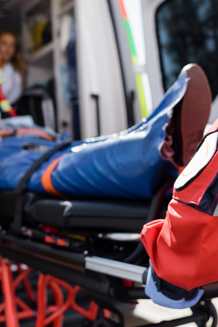 Selective focus of paramedic in uniform carrying stretcher with patient in ambulance ca outdoors