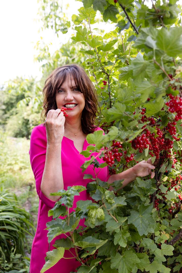Eine Frau im pinkfarbenen Kleid isst rote Johannisbeeren vom Strauch.