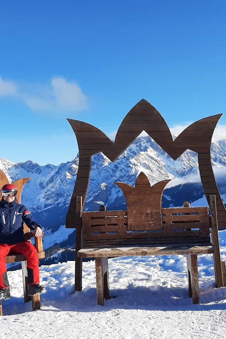 Ein Skifahrer sitzt auf einem Thron vor einer verschneiten Berglandschaft.