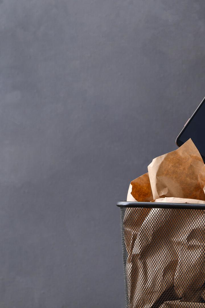 Closeup view of woman throwing smartphone into trash bin on grey background, space for text. Digital detox concept